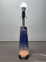 26-inch blue tapered textured glass table lamp on a metal base with LED bulb lit, showing color gradient from dark blue to lighter blue/white at base.