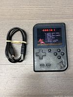 Front view of handheld game console powered on showing 400 in 1 game menu and USB charging cable