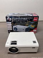 Projector with box for RCA RPJ199 Combo Home Theatre Projector bundle showing 2-in-1 combo with fold-up screen and listed features such as Bluetooth, LED light source, USB, HDMI ports, and built-in speaker.