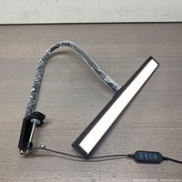 Full view of the LED desk lamp showing the rectangular light panel, flexible neck wrapped in plastic, and sturdy clamp for mounting.