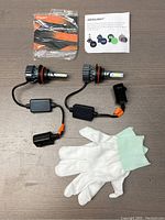Top view of two LED headlight bulbs with wiring connectors, installation manuals, and white cotton gloves on a wooden surface.
