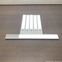 Six LED magnetic auto light bars arranged on wooden surface. Five have white LEDs, one appears powered off or with warmer LED light.