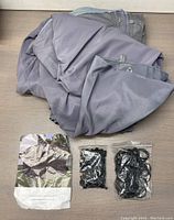 Photo of folded gray tent cover fabric along with plastic bags containing black bungee cords and plastic rings for assembly.