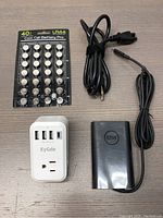 Top view of the coin cell batteries, 65W AC adapter with detachable cord, and travel plug adapter arranged on a surface.