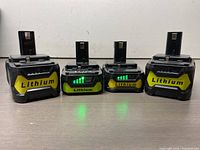 Four lithium-ion 18V power tool batteries arranged side by side, showing front with 'Lithium' yellow label and charge indicators on two units.