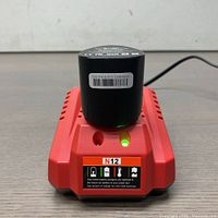 Front view of the red charger with black lithium-ion battery inserted, green indicator light on
