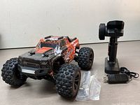 Remote control monster truck alongside remote controller, USB cable, and spare parts bags on a light wood surface.