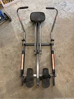 Top view showing padded seat on sliding rails, adjustable handlebars with foam grips, and footrests with straps in place.