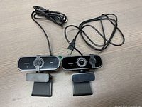 Two USB HD webcams side by side, each with a clip mount and long USB cable, placed on a wooden surface.