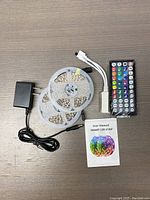 Two rolls of LED strip light, power adapter, controller cable, remote control, and user manual arranged on surface