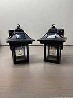 Pair of black solar outdoor lantern lights shown from the side view, highlighting the lantern design with a loop at the top.