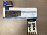 Top view showing the full-sized Insignia Bluetooth keyboard box, Arrow RGB LED lights box, and HDMI to VGA adapter box arranged on a table.