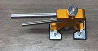 Gold-colored dent puller tool with two metal handles and rubber clamps on a wooden surface.