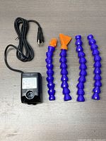 Photo of water pump with power cord and four flexible segmented extension tubes including two orange nozzle heads.