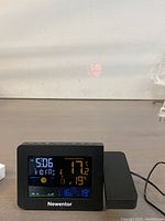 Front view of the Newentor wireless atomic weather station showing time, date, and weather information clearly on the color screen, with power cord plugged in.