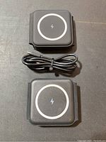 Two black wireless charging docks with USB-C cables on a flat surface, showing the top circular charging area with a lightning bolt icon.
