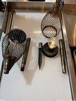 Four solar garden lamps disassembled showing the lantern-style mesh metal outer casing with light bulb inside, and metal stakes for ground installation.