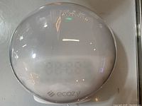 Front view showing round Ecozy wake-up light with digital clock display visible through frosted cover.
