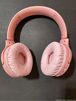 Full view of pink over-ear Bluetooth headphones laid flat showing headband and cushion pads.