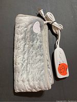 Electric heating pad folded neatly showing the fabric material and the attached controller cord.