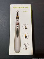 Full front view of the massager pen box showing the device body with digital screen and three different interchangeable massage heads.