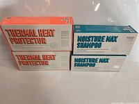 Two boxes each of Thermal Heat Protector and Moisture Max Shampoo stacked in sets of two, showing packaging and product names.