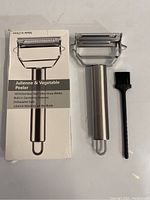 Photo showing the peeler and cleaning brush alongside the product box which states features like 100% stainless steel, ultra sharp blades, built-in garnishing features, dishwasher safe, and lifetime warranty on blade.