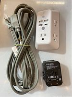 Overview of the bundle showing multi-plug outlet expander with USB ports, three coiled power cords with 3-prong plugs, and a black surge protector adapter