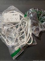Photo of two extension cord power bars sealed in plastic bags, showing the white and black strips with their cords coiled.