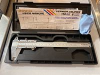 Open case holding the stainless steel Spurtar Vernier Caliper, user manual inserted in lid, and blue cleaning cloth in corner.