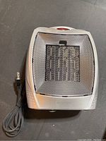 Front view of silver ceramic space heater showing metal mesh grille and attached power cord.