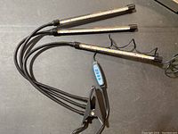 Triple-arm LED grow light with black clamp base and flexible arms with LED bars attached, shown laid flat on surface.