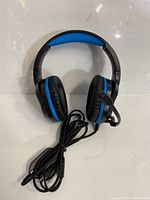 Front view of black and blue padded over-ear wired gaming headphones with attached adjustable microphone and long cable.