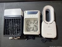 Three mini tower fans arranged side by side on a black surface showing front views and power cords.