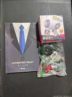 LCD writing tablet box, mini drone in plastic packaging, and bubble blower box together on gray surface