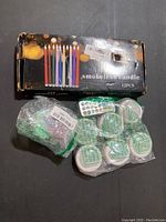 Box of 12 LED smokeless candles with colorful candle design and some accessories including remote control visible in packaging.