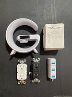 Top view of wireless charger speaker, two wall outlets (white and black), universal travel adapters in box and loose.