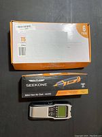 Box of six SpeePlant T5 grow light bulbs, Seekone Mini Hot Air Gun HG350 box and digital stud finder on a dark surface.