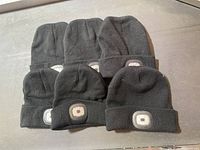 Six black knit toques laid out flat, arranged in two rows of three, displaying the front LED light modules on each.