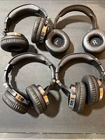 Four black over-ear headphones arranged in a cluster showing the padded ear cups and adjustable headbands with metallic hinges on ear cups.