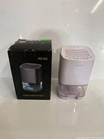 Photo of mini dehumidifier model H2102 next to its black retail box displaying the dehumidifier image and model number.