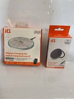 Two wireless charging pads in their original packaging. Left is a white marble IQ wireless charging pad in a box, right is a black IQ wireless charger box with built-in magnet.