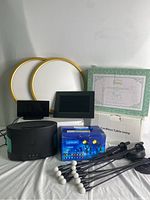 Photo showing multiple household items including 2 round ceiling lights with golden rims, various digital photo frames, a box of LED landscape lights, and black essential oil diffuser.