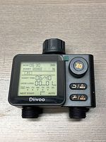 Top front view of Divoo water timer showing LCD screen with watering schedule, control buttons and OK button on right side, dual water outlet ports at bottom