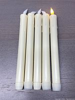Top and side view of 5 cream-colored electric flameless candles assembled in a row, one candle lit showing realistic flickering LED flame.