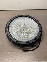 Front view of first 100W UFO High Bay LED light showing black metal housing with ventilation holes and LED array.
