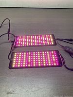 Two Barina LED light panels side by side powered on showing LED grids of red, white, and yellow lights on a dark surface.