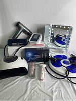 Photo showing entire health and wellness bundle containing massage tool, UV nail lamp, blood pressure monitor, ophthalmoscope, vanity mirror with lights, facial hair remover, razor, twist waist disc board, and thermometer.