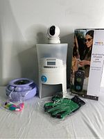 Photo of the pet feeder, security camera, grooming glove, Bluetooth speaker box, and purple cat toy with plastic wrap protective covering.