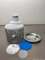 Front view of the pet water dispenser with water bottle, clear reservoir, white top, disassembled filters and metal lid displayed separately in front.